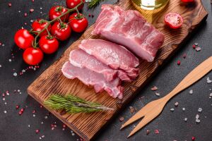 Свежесрубленное мясо на деревянной разделочной доске, украшенной розмарином, с рядом красными помидорами черри