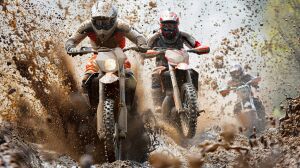 Два гонщика в полной экипировке, покрытые грязью, мчатся по скользкой трассе