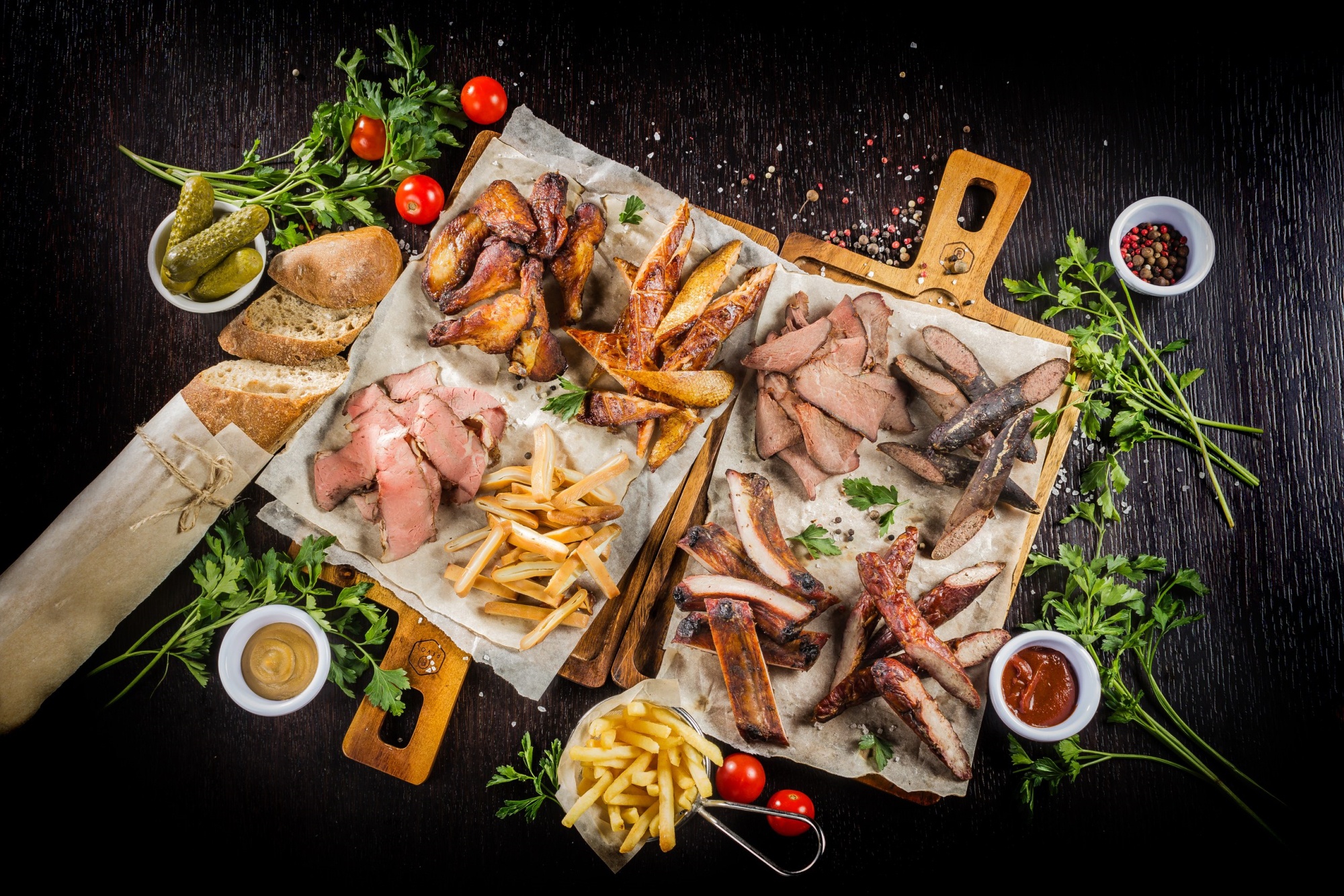Сытное угощение на деревянной доске: копченое мясо, картофель фри, свежие томаты черри и соусы