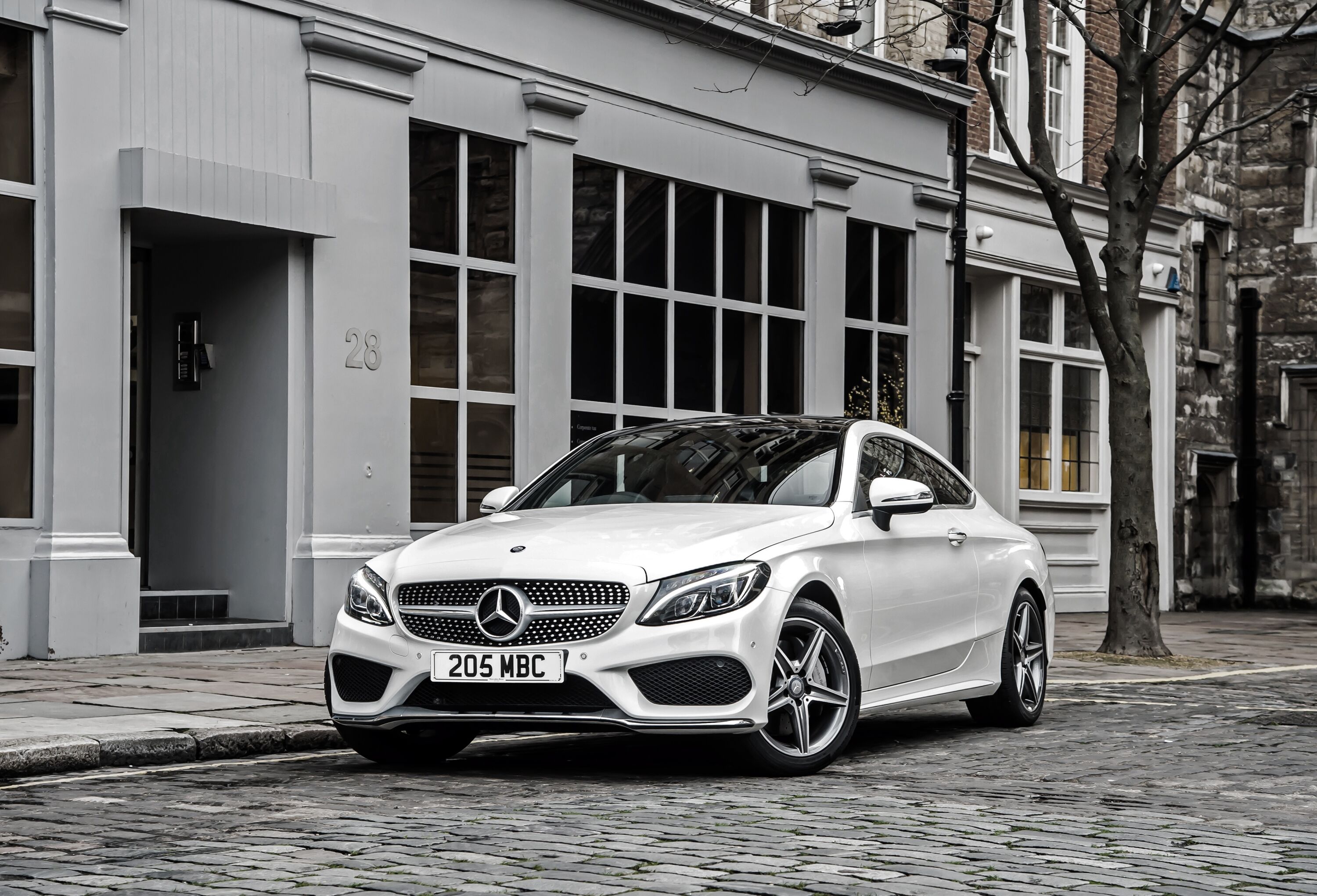 Элегантный белый Mercedes-Benz C-Class в солнечном свете, припаркованный на мощенной улочке