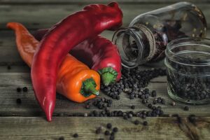 Яркие перец чили, разбросанные перец горошек и старая стеклянная банка на деревянном фоне