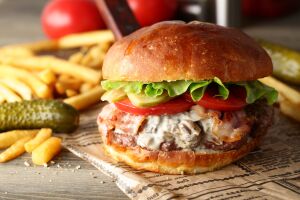 Сочный бургер с хрустящими картофелем фри и маринованными огурчиками на фоне газетной бумаги