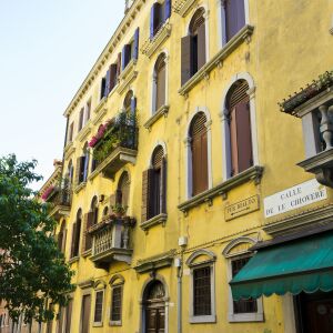 Солнечный день на венецианской улице: фасад дома, украшенный цветами в кашпо, детализированные окна, зеленая вывеска и тихая атмосфера