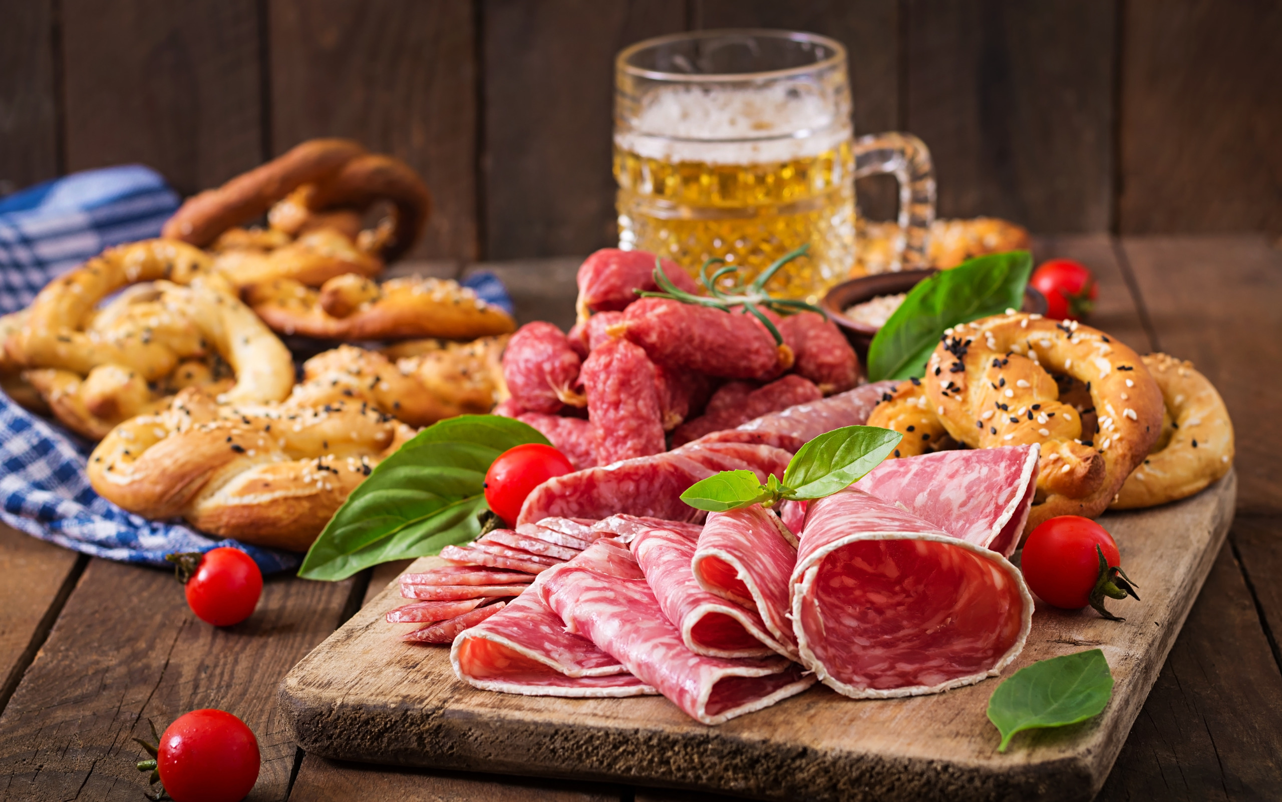 Вкусное угощение из свежих колбасок, ароматных пряников, хрустящих кренделей и освежающего пива на деревянной доске