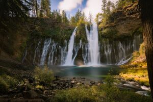 Каскад водопада, окруженный пышной зеленью и солнечными лучами, проникающими сквозь листву