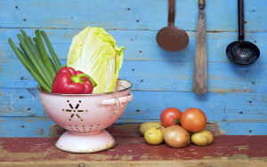 Сочные овощи и зелень в розовой дуршлаге на деревянном столе